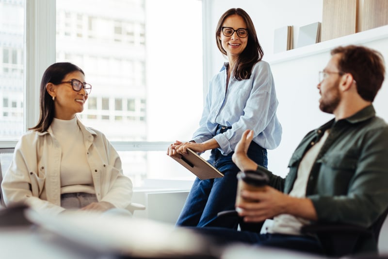 2 women and 1 man sitting together talking in workplace